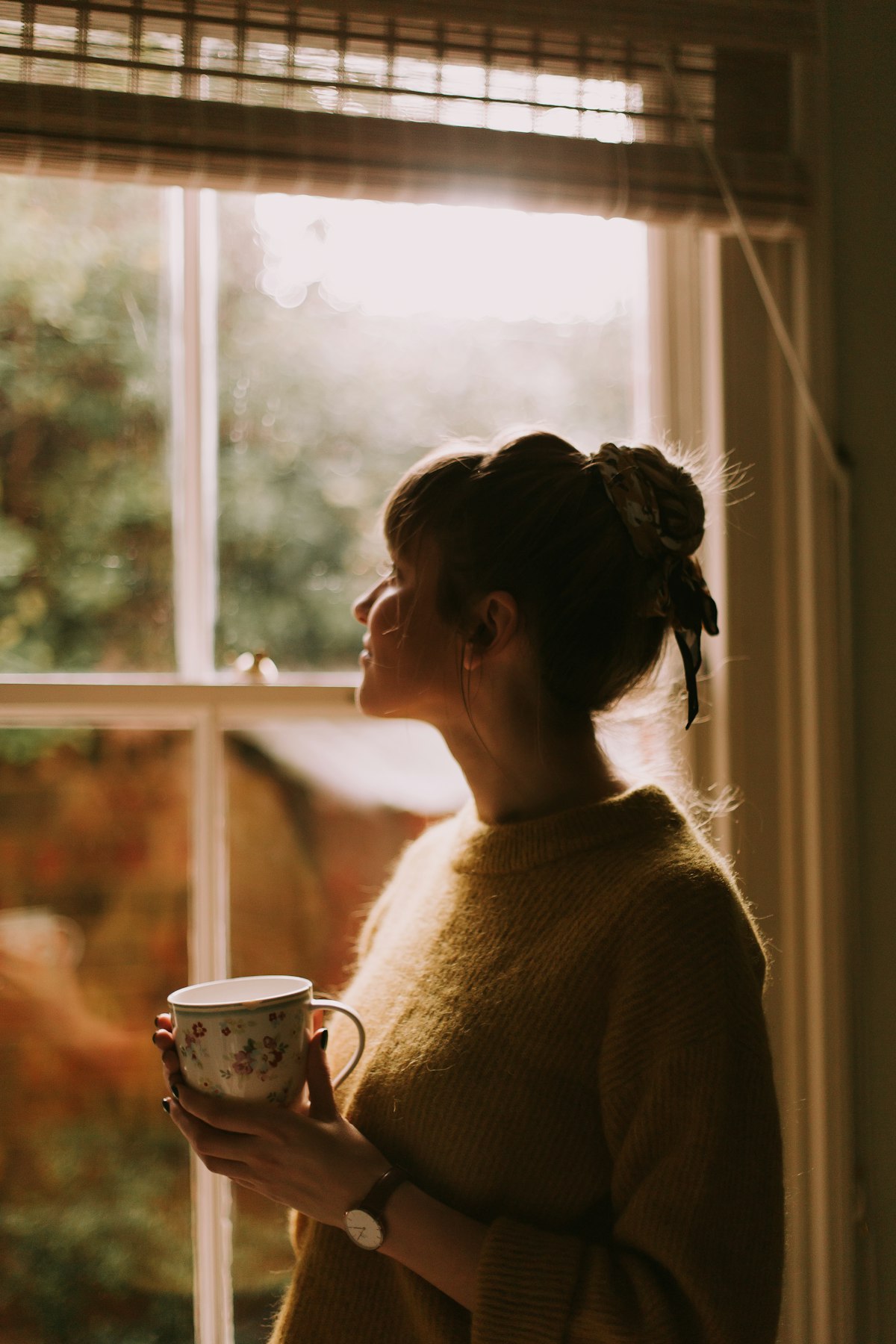 A woman pausing with a warm cup of tea by a window